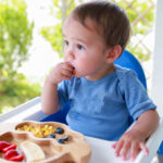 A toddler sits in a high chair with a nutritious meal.